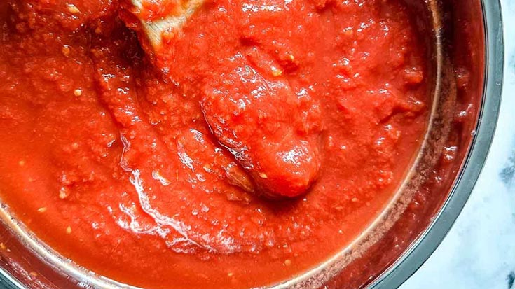 A closeup of marinara in a pot with a wooden spoon.