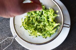 Sprinkling salt over grated cucumber in a mesh sieve.