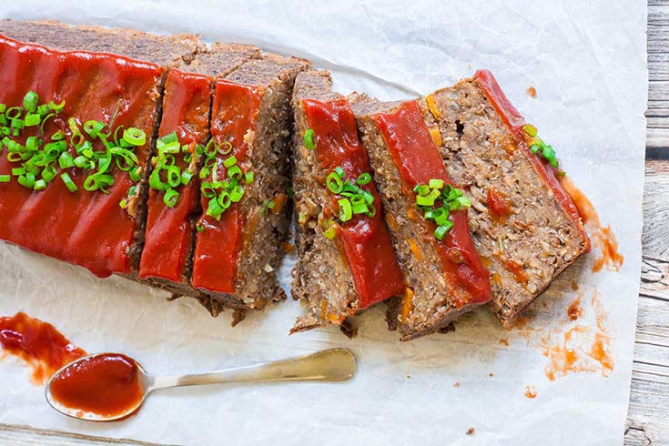 An overhead view of a vegan lentil loaf sliced and covered in sauce.