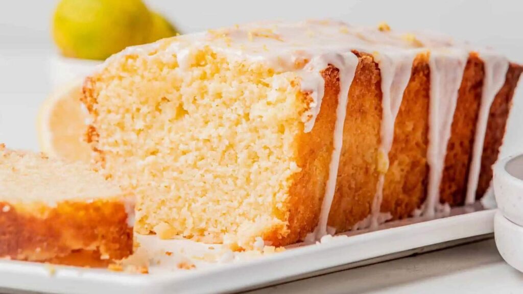 A closeup of a pound cake on a white platter with one slice taken from the front side.