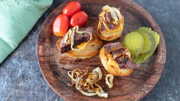 Three venison brisket crostini on a wood plate.