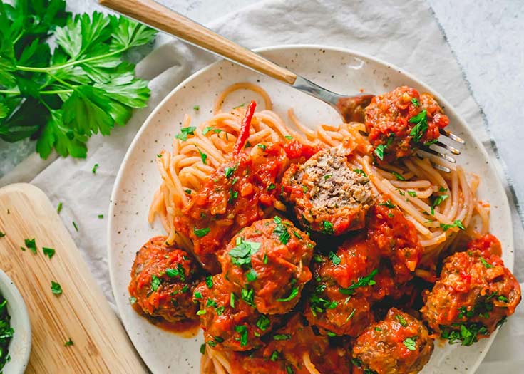 A white plate holds a pile of venison meatballs served over spaghetti.