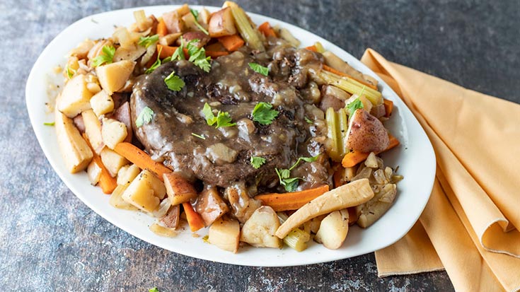 A white, oval platter holds a venison roast surrounded by vegetables.