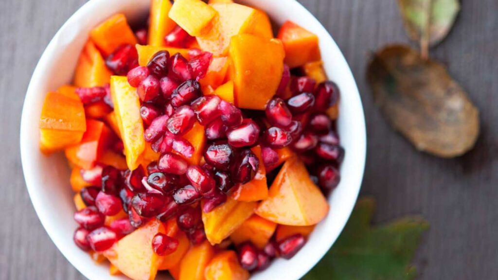 A white bowl filled with winter harvest fruit salad on a wood surface.