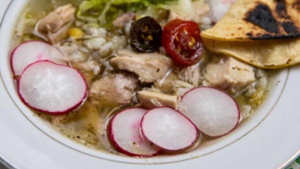 Green Chicken Pozole in a white bowl with slices of radishes on top.