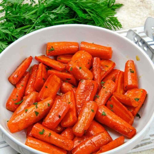 Air fryer carrots in a white bowl with carrot greens behind it.