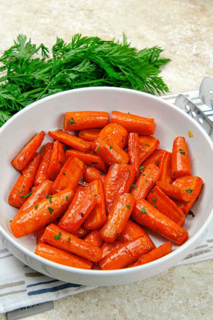 Air fryer carrots in a white bowl with carrot greens behind it.