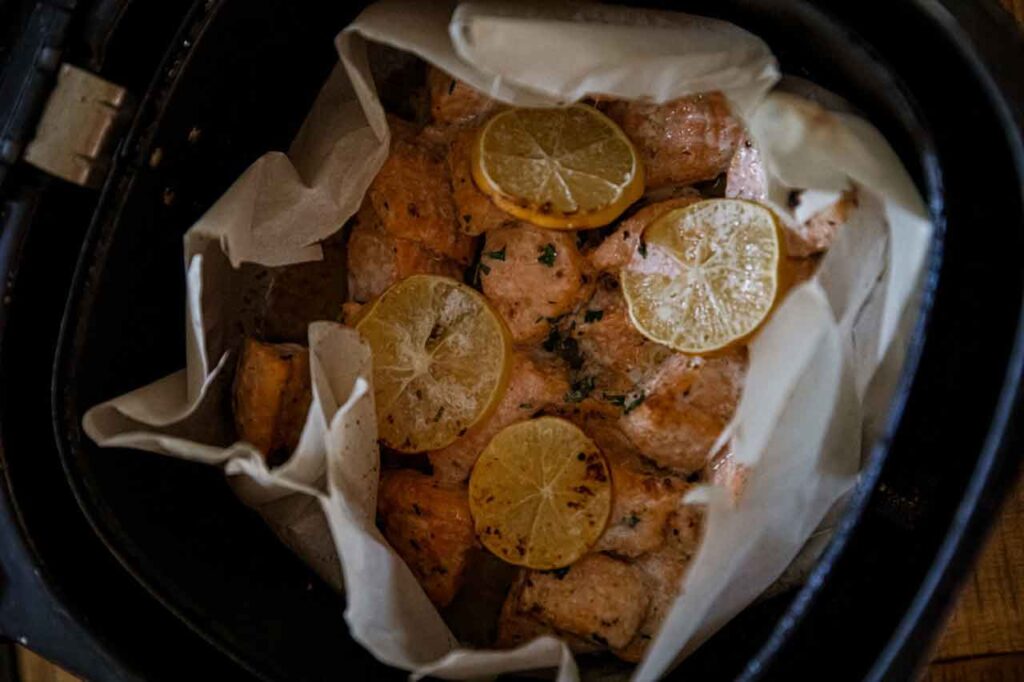 A parchment-lined air fryer basket filled with salmon bites.