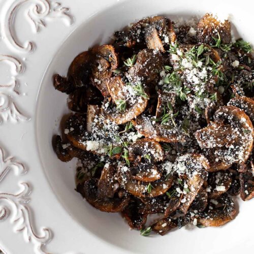 An overhead view of air fryer baby bellas in a white bowl with parmesan and herbs sprinkled over the top for garnish.