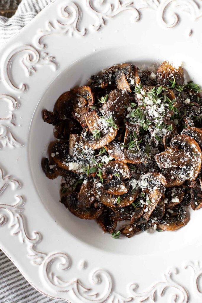 An overhead view of air fryer baby bellas in a white bowl with parmesan and herbs sprinkled over the top for garnish.