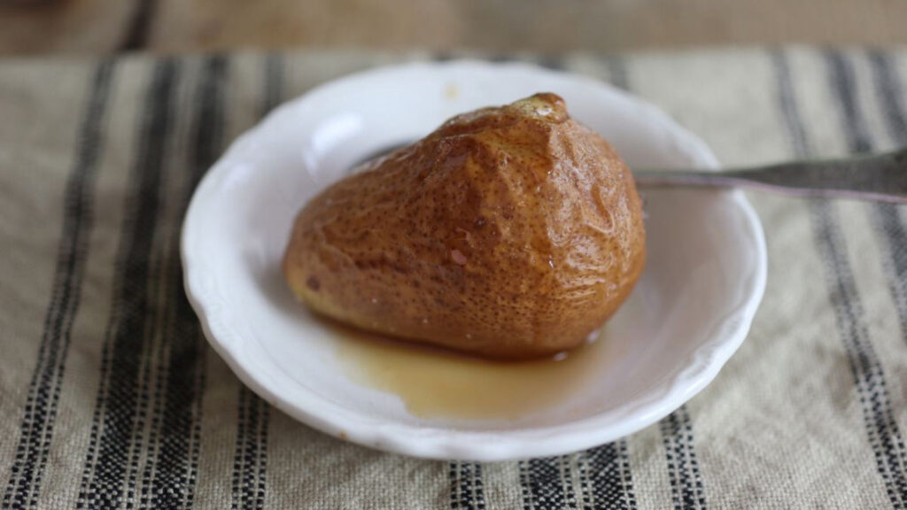 A single baked pear in a small white dish with a spoon.