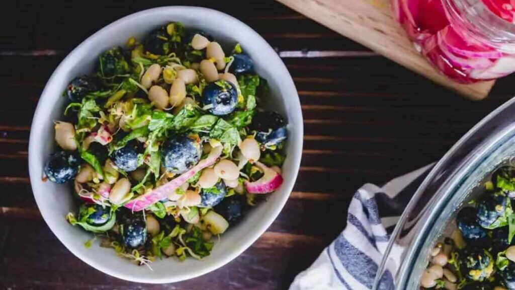 A bowl filled with blueberry white bean salad on a wood surface.