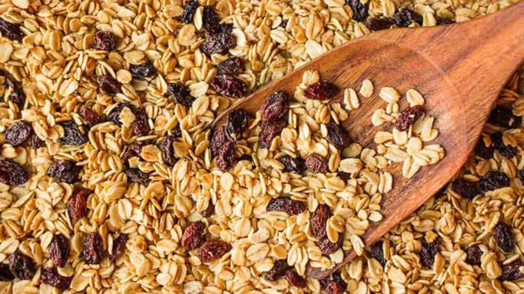 A closeup of Cinnamon Raisin Granola With Coconut Oil, with a wood scoop resting in it.