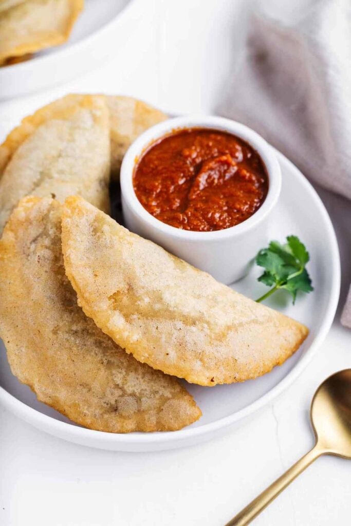 Empanadas on a white plate with red dipping sauce.