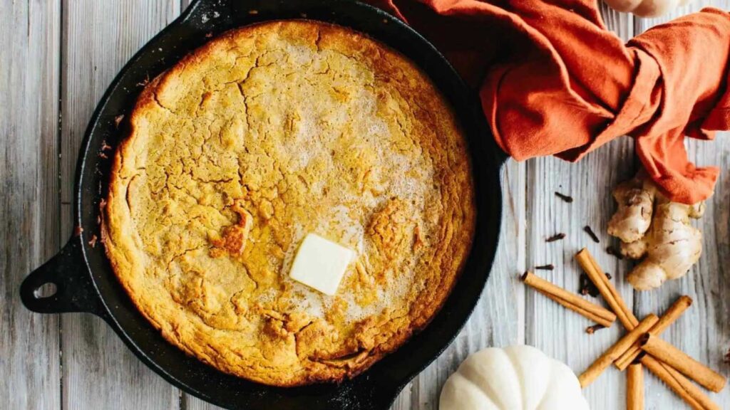 An overhead view of an oatmeal pumpkin dutch baby in a cast iron skillet. A pat of butter melts on top of the Dutch baby.