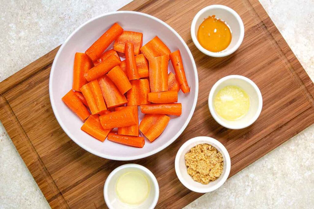 Air fryer carrots recipe ingredients in individual bowls sitting on a cutting board.