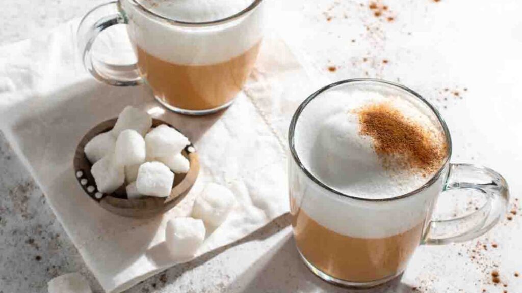 Two glass mugs filled with red cappuccino. Sugar cube sit in a small bowl next to them.