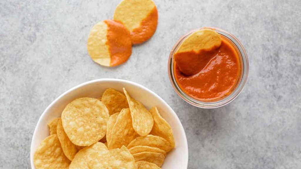 A small bowl full of salsa roja with a white bowl of chips next to it.