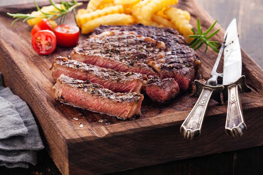 An air fryer ribeye steak, sliced on a cutting board.
