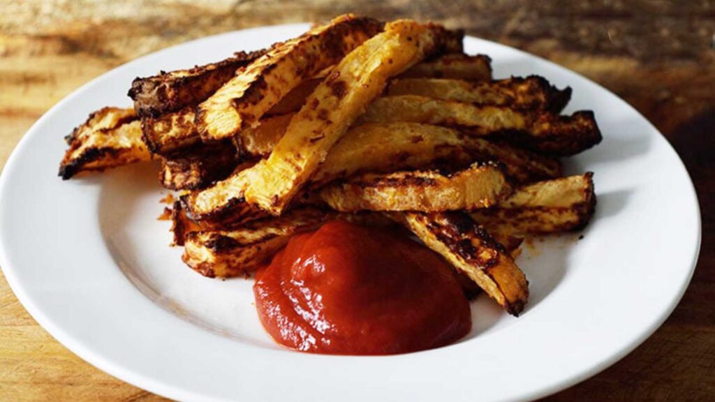 Just-cooked Air Fryer Rutabaga Fries laying on a white plate with some ketchup.