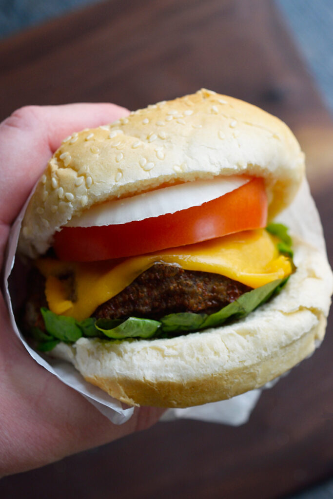 A hand holds an Air Fryer Turkey Burger wrapped in parchment over a cutting board.