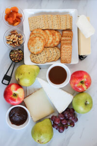 Ingredients for this Fruit And Cheese Charcuterie Board Recipe, gathered on a white marble surface.