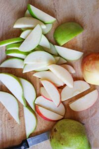 Sliced apples and pears laying on a cutting board with a knife.