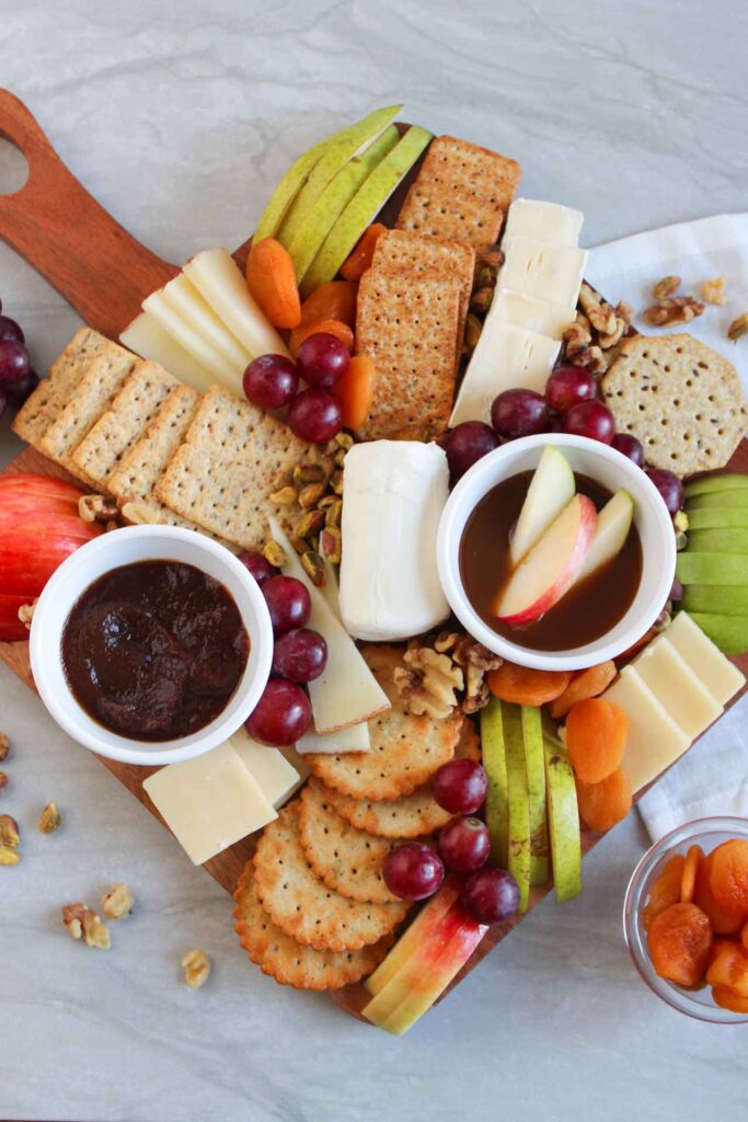 An overhead view looking down on a fruit and cheese charcuterie board on a marble surface.