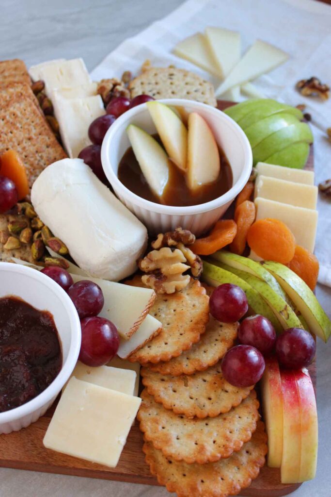 A side view of a charcuterie board filled with dip, apples, grapes, pears, cheeses and crackers.