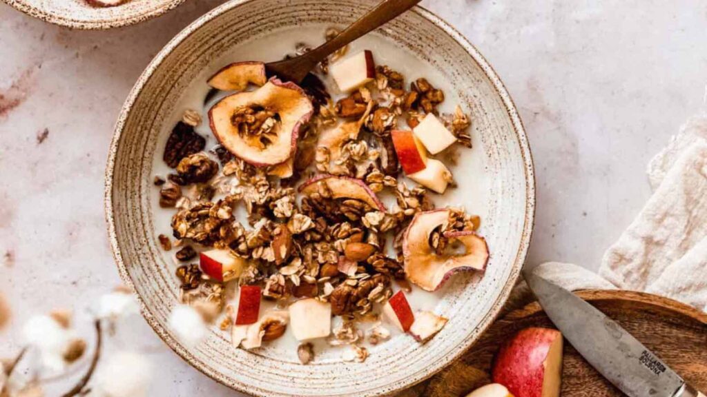 An earthen bowl filled with milk and applesauce granola.