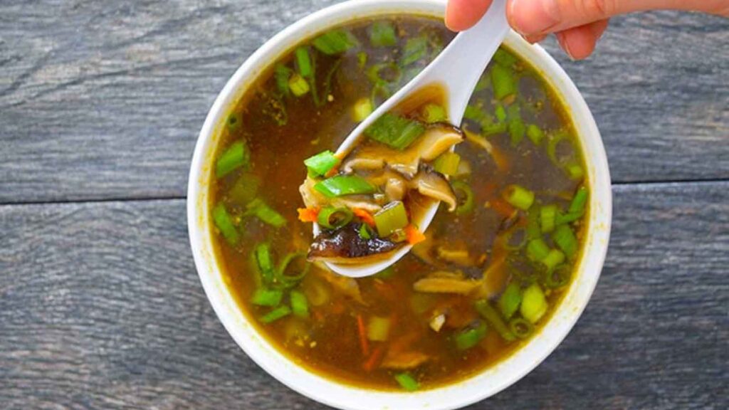 Shiitake Mushroom Soup served in a white bowl. A hand lifts a spoonful of it out of the bowl.