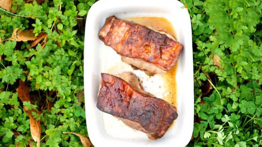 Asian Style Pork Chops in a white casserole dish sitting in the midst of some greenery.