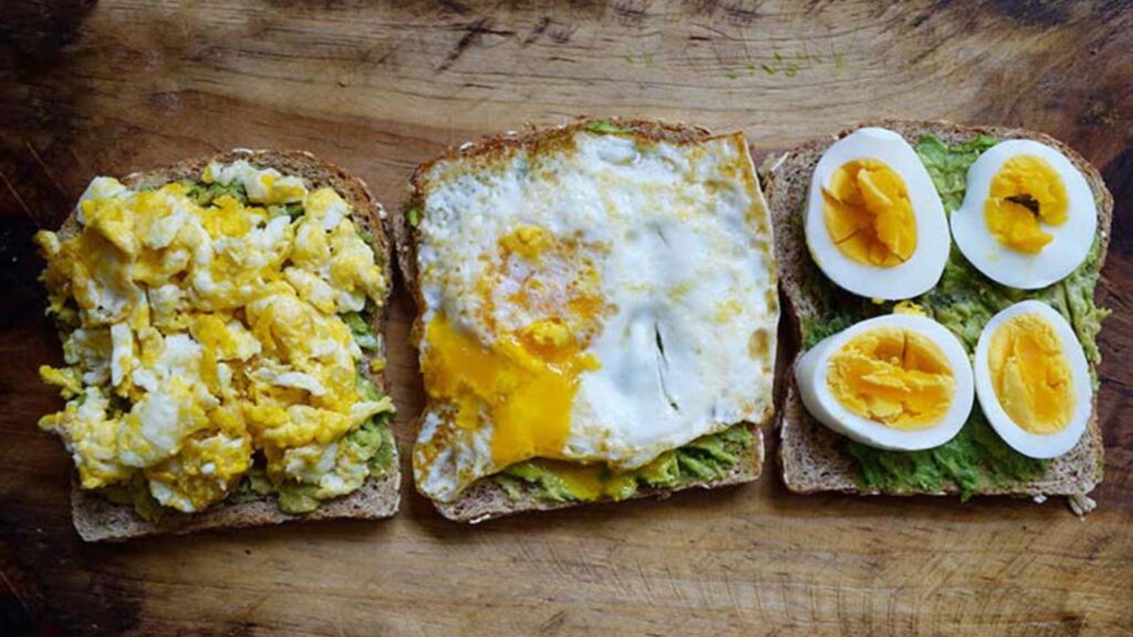 A lineup of three slices of bread. One with scrambled eggs, one with a fried egg and one with hard-boiled egg slices.