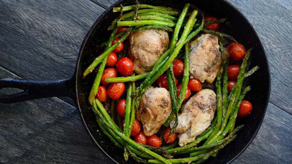 A black, cast iron skillet holds this just-cooked, Oven-Baked Chicken Thighs Recipe With Veggies