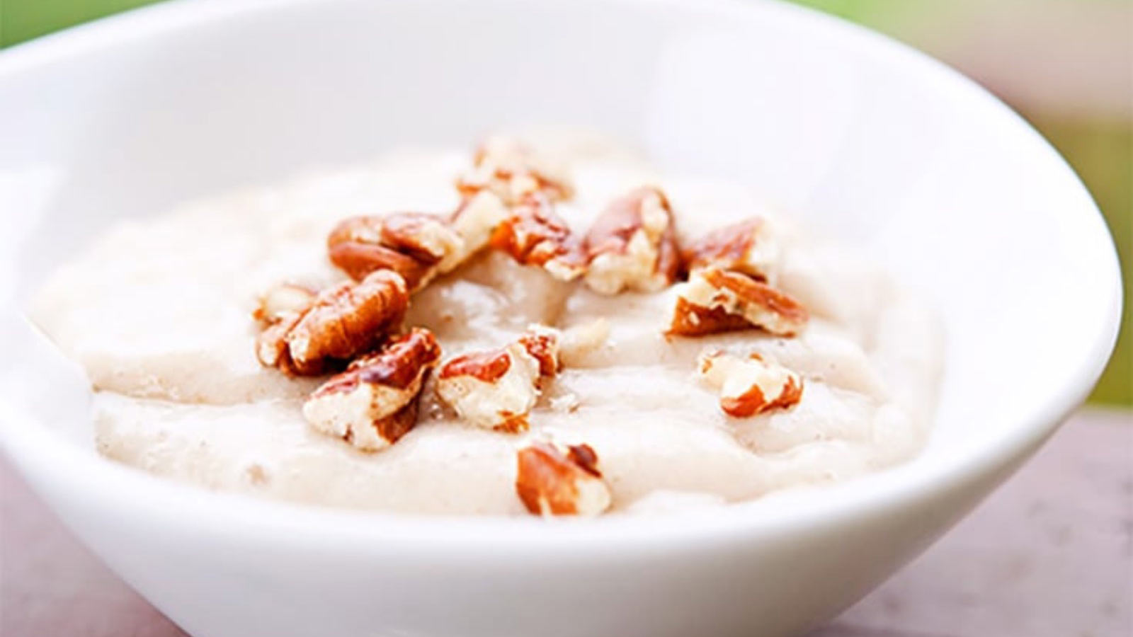A side view of a white bowl filled with banana pudding and topped with chopped nuts.