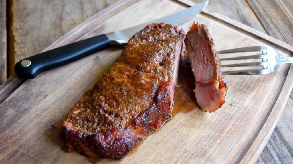 A piece of steak on a cutting board with one piece cut off.