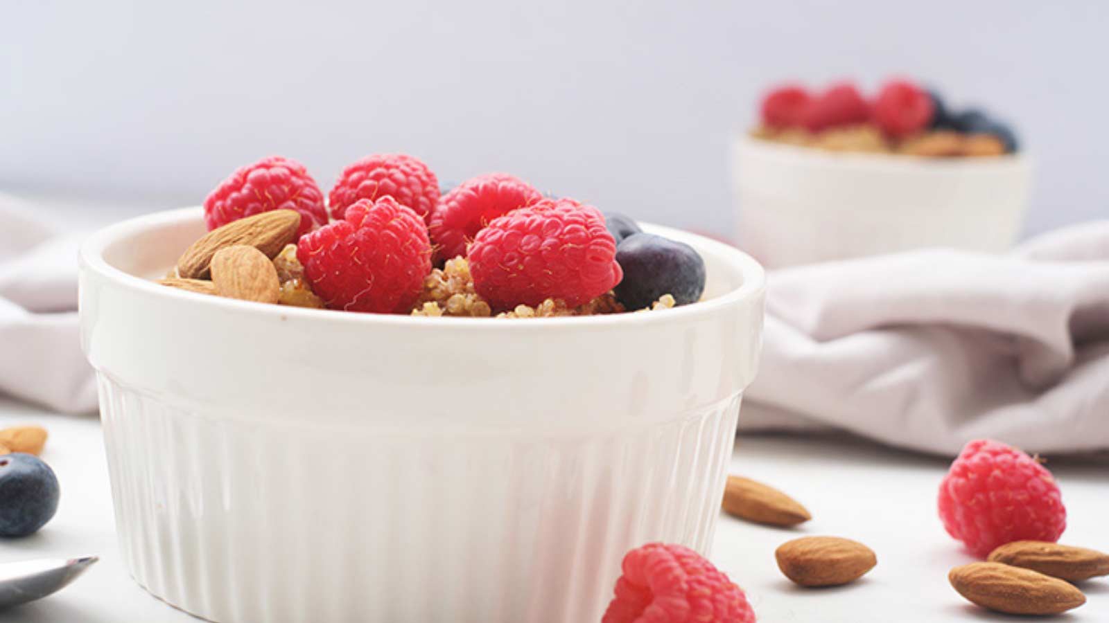 A white bowl of Breakfast Quinoa with fresh raspberries and blueberries.