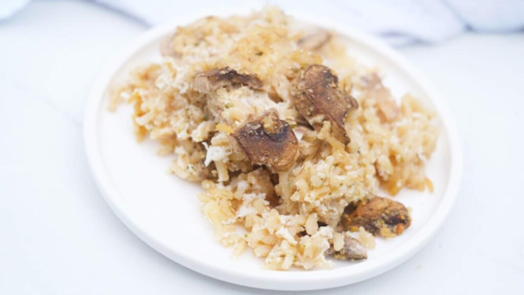 A white plate filled with brown rice mushroom casserole, sits on a white table.