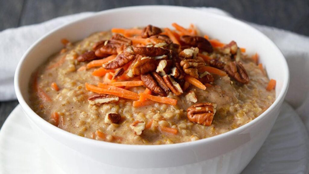 Carrot Cake Oatmeal poured into a white bowl and garnished with fresh grated carrots and chopped pecans.