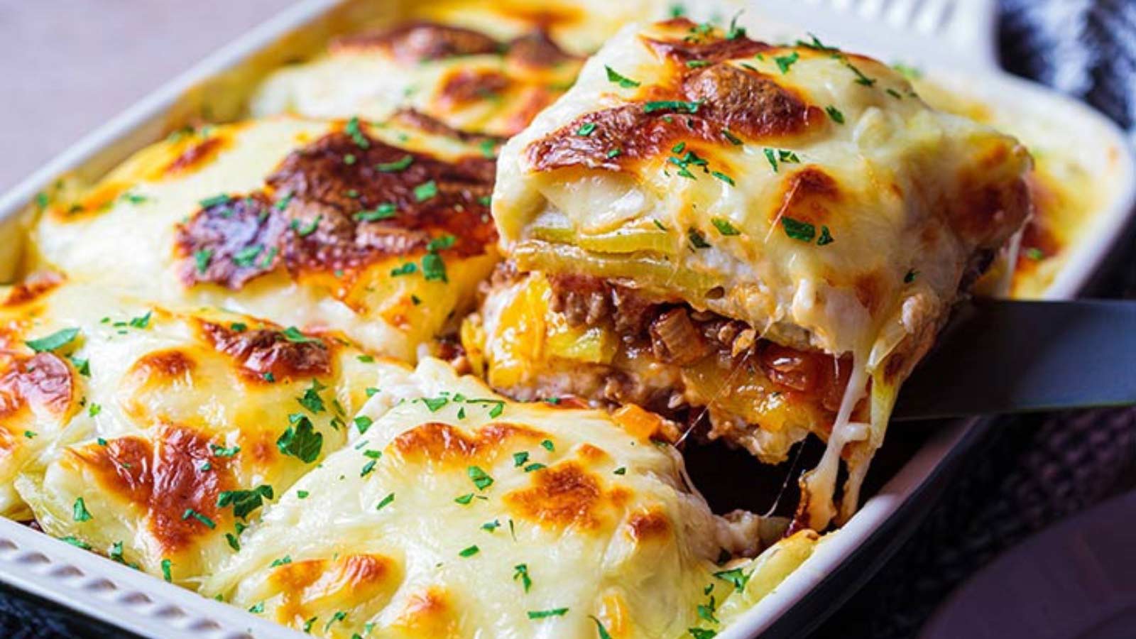 A spatula lifts a portion of lasagna out of a casserole dish of lasagna.