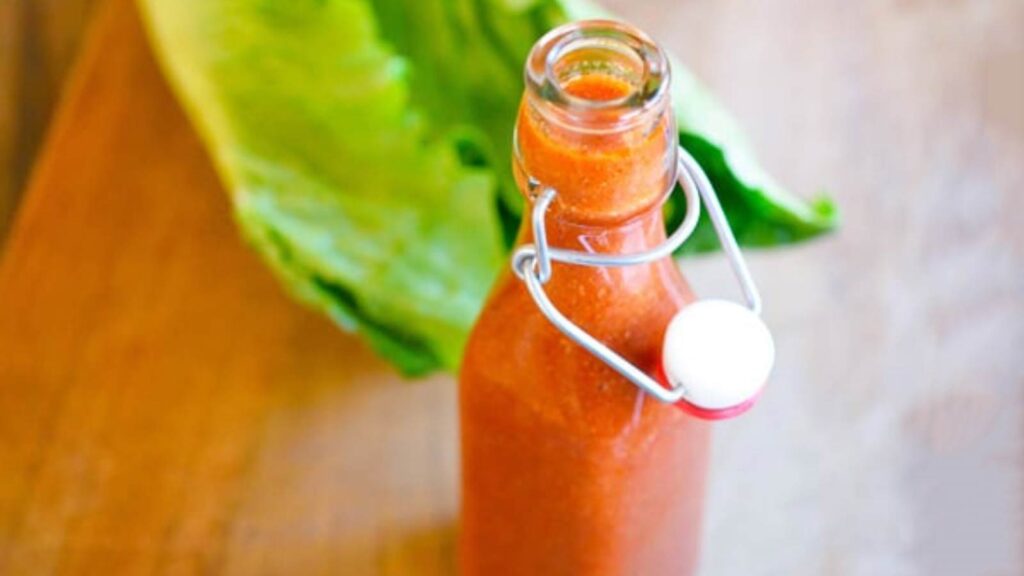 An open bottle of homemade Catalina Dressing on a table next to some lettuce.