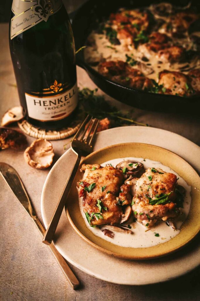 A table setting with a plate of Champagne chicken. A bottle of Champagne sits on the table.