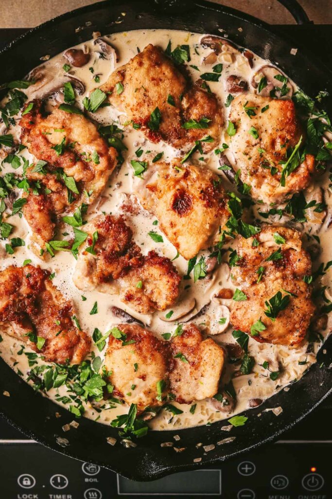 Fresh parsley sprinkled over the chicken in a pot of cream sauce.