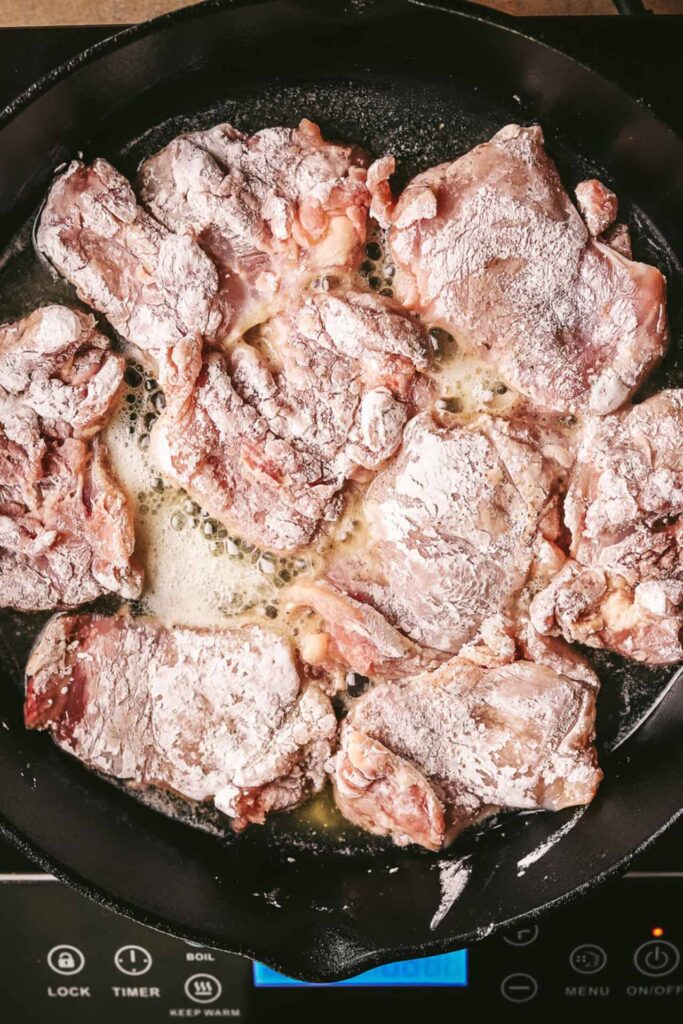 Floured chicken thighs in a buttered cast iron skillet.