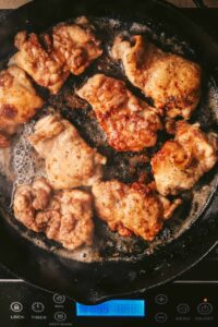Cooked chicken thighs, cooked and laying in a cast iron pot.