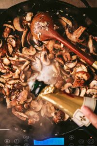 Adding champagne to the pot of mushrooms, onions and garlic.