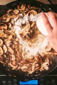 Adding cream to mushrooms in a pot.