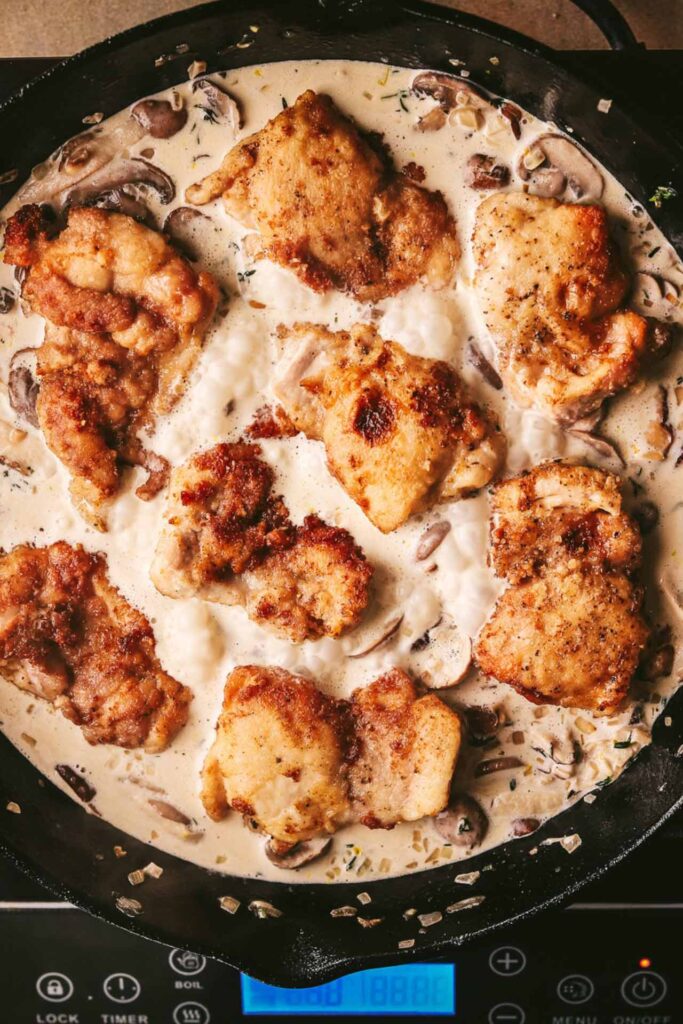 Cooked chicken thighs added back into the pot with cream sauce.