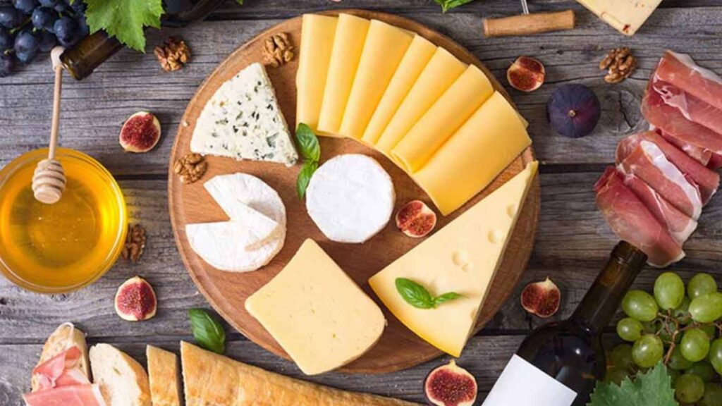 An overhead view of a cheese platter with wine, honey and bread laying around the platter.