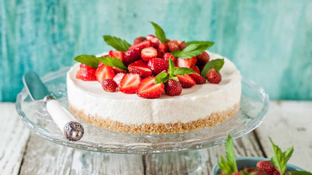 A whole cheesecake, topped with fresh strawberries and mint, sitting on a cake stand.